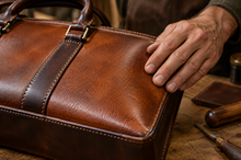 Main posée sur une sacoche ordinateur en cuir pleine fleur cognac aux coutures sellier